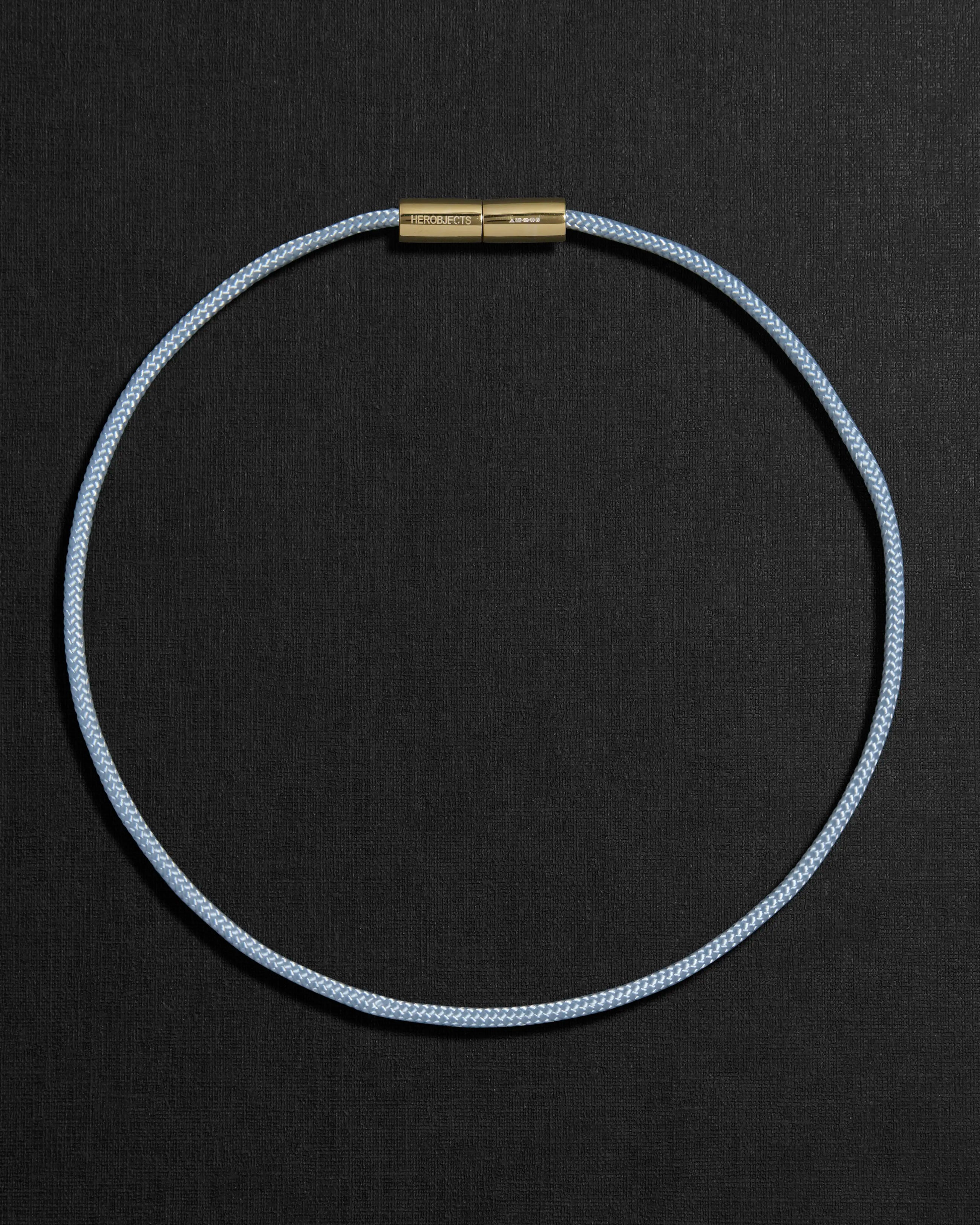 Blue cord necklace with a 18K gold clasp on a black background