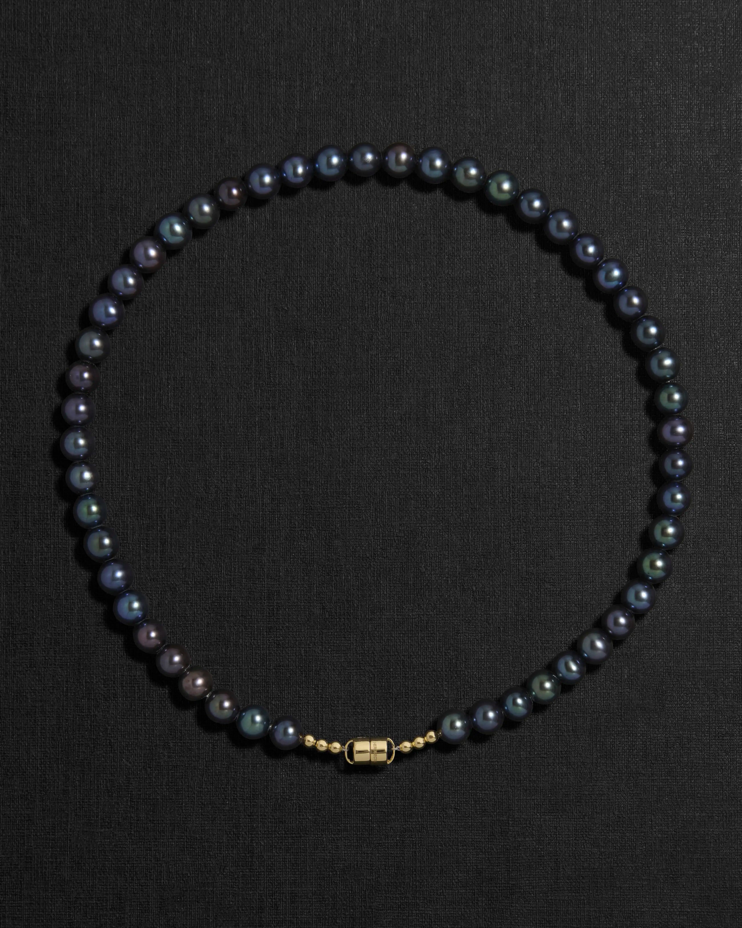 Black pearl necklace with a 18K gold clasp on a black background