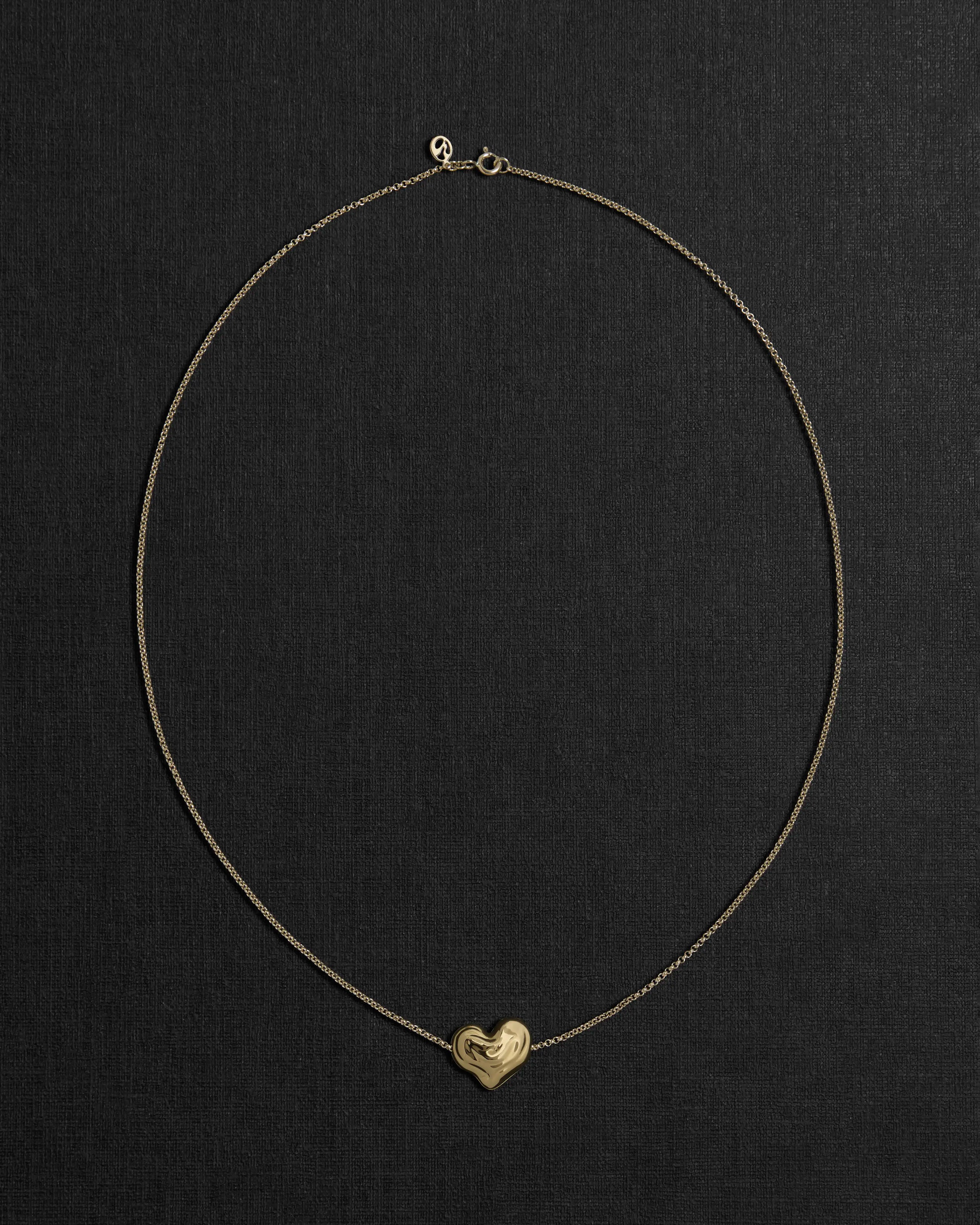 18K gold rollo chain necklace with a heart-shaped pendant on a black background