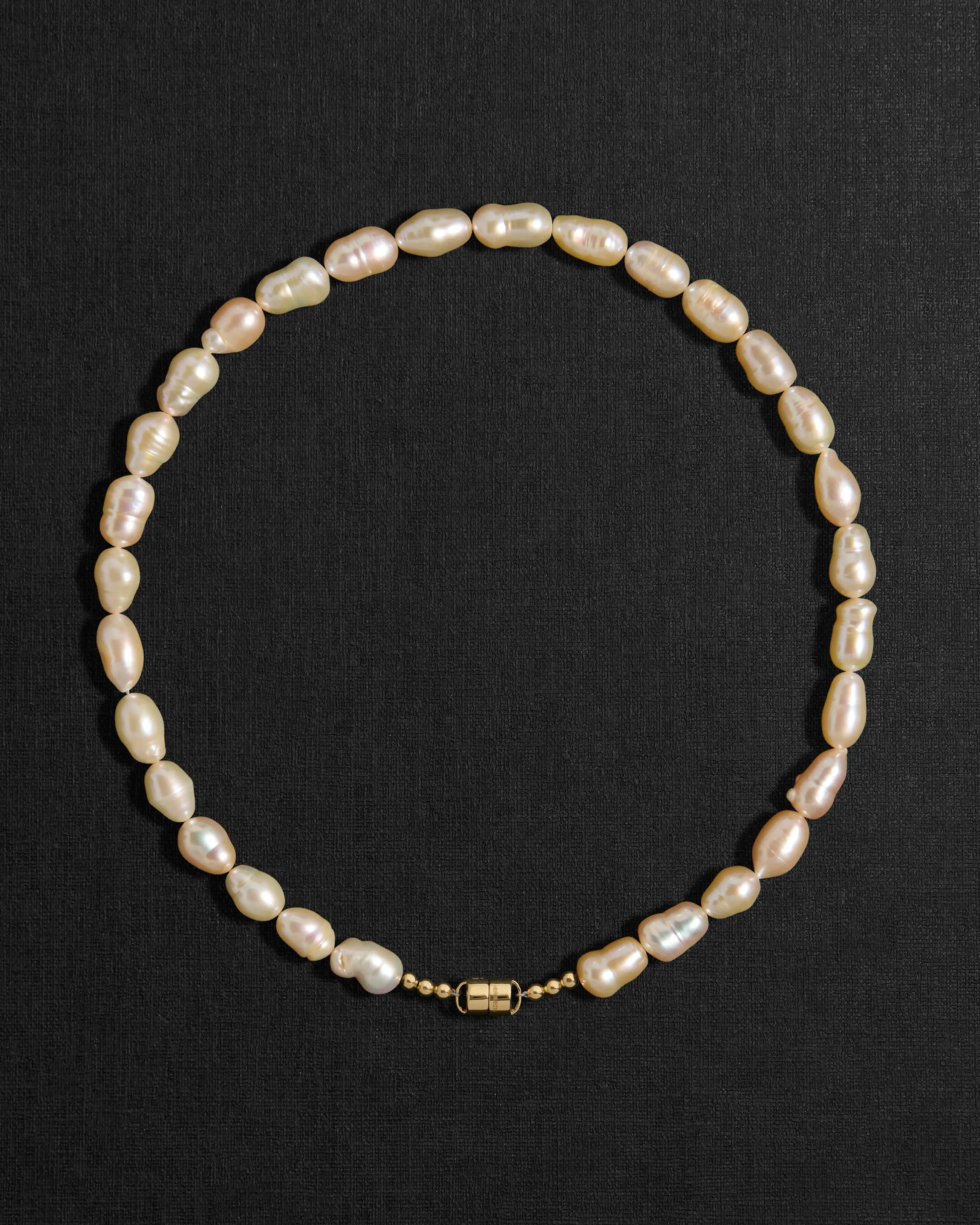 Peach pearl necklace with a 18K gold clasp on a black background