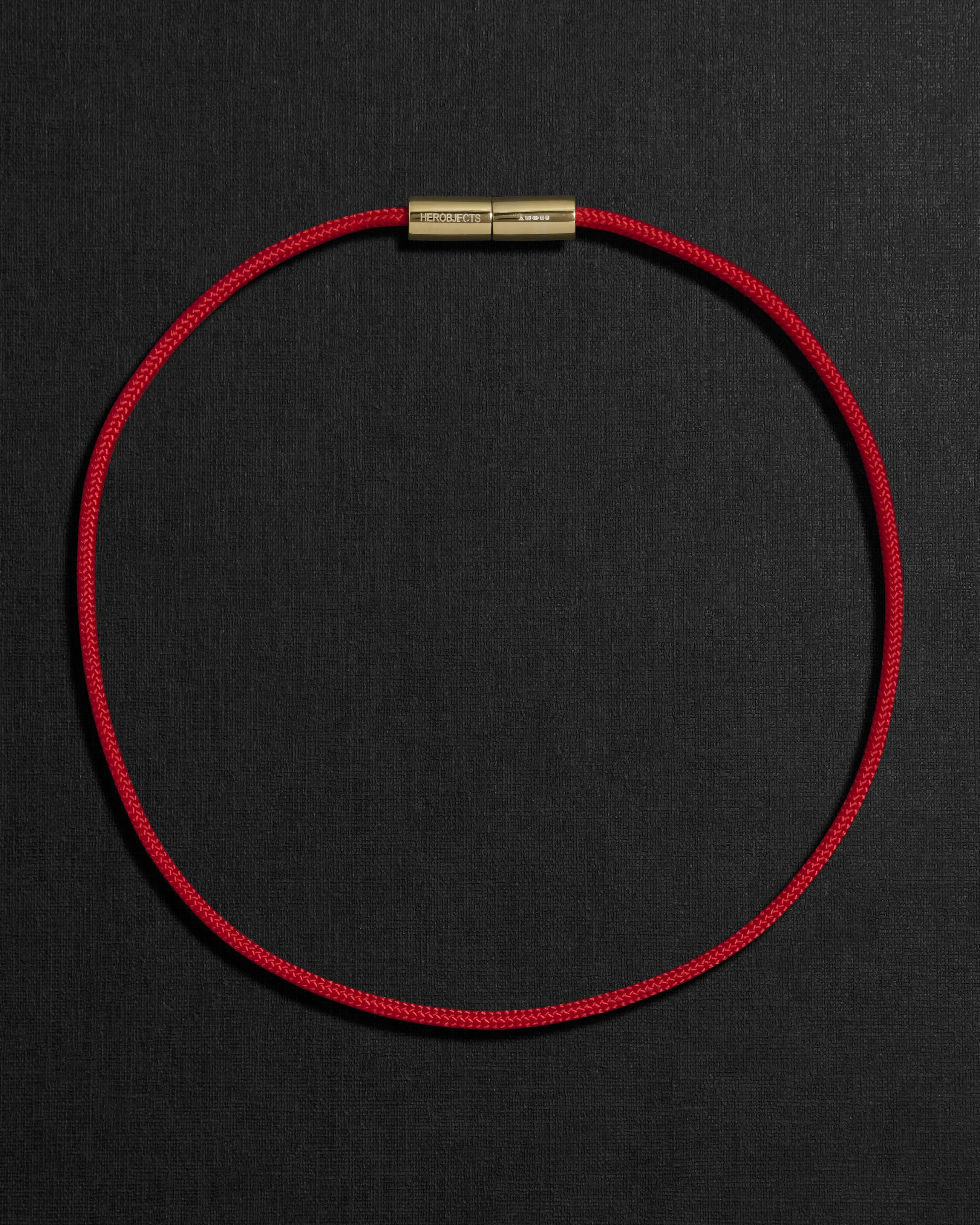 Red cord necklace with a 18K gold clasp on a black background