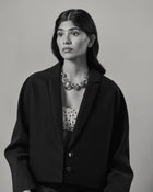 A black and white portrait of a model wearing a black cropped blazer over a white top with black polka dots, accessorized with all 18K Gold Hero objects.