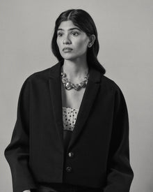 A black and white portrait of a model wearing a black cropped blazer over a white top with black polka dots, accessorized with all 18K Gold Hero objects.