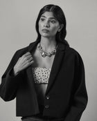 A black and white portrait of a model wearing a black cropped blazer over a white top with black polka dots, accessorized with all 18K Gold Hero objects.