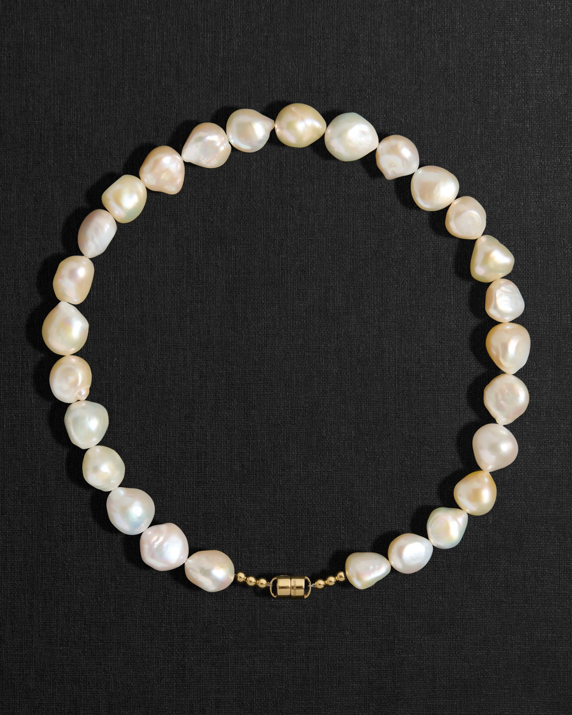 Ivory pearl necklace with a 18K gold clasp on a black background