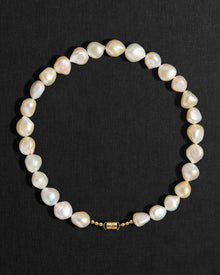 Ivory pearl necklace with a 18K gold clasp on a black background