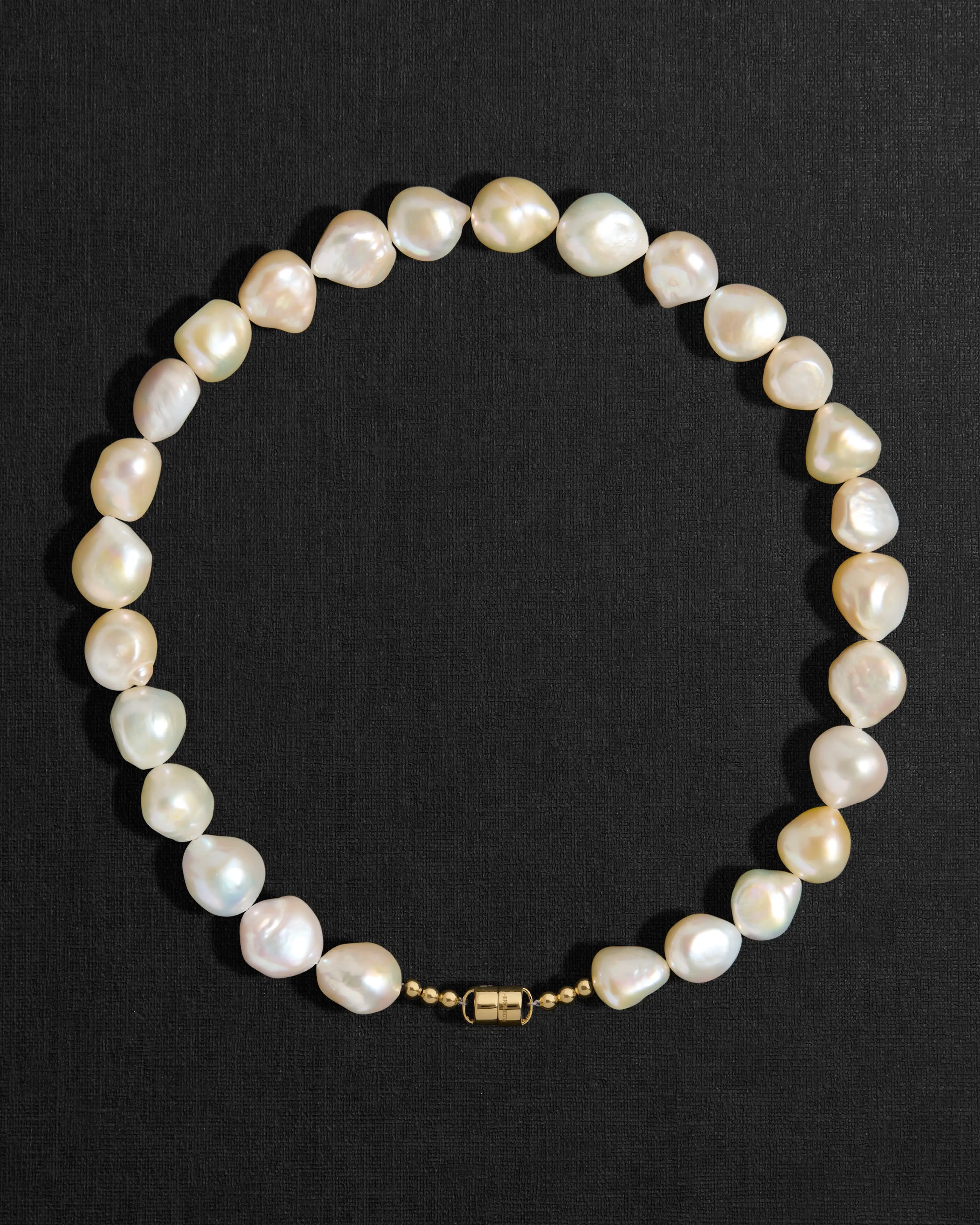 Ivory pearl necklace with a 18K gold clasp on a black background