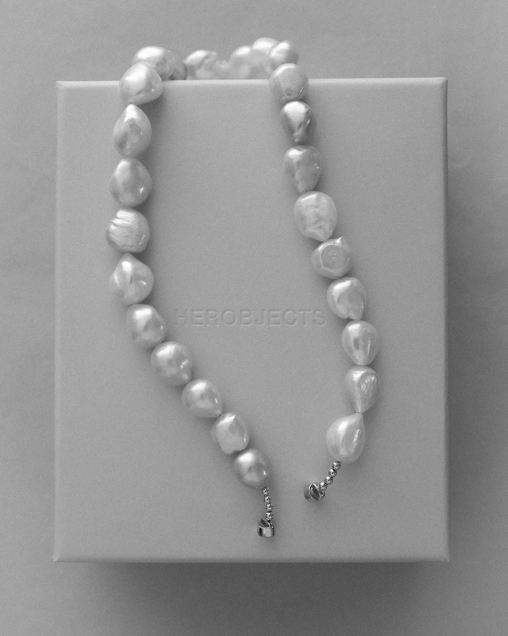 A strand of irregular 18K gold baroque pearls draped over a pink signature HEROBJECTS rectangular box.
