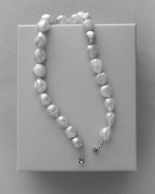 A strand of irregular 18K gold baroque pearls draped over a pink signature HEROBJECTS rectangular box.