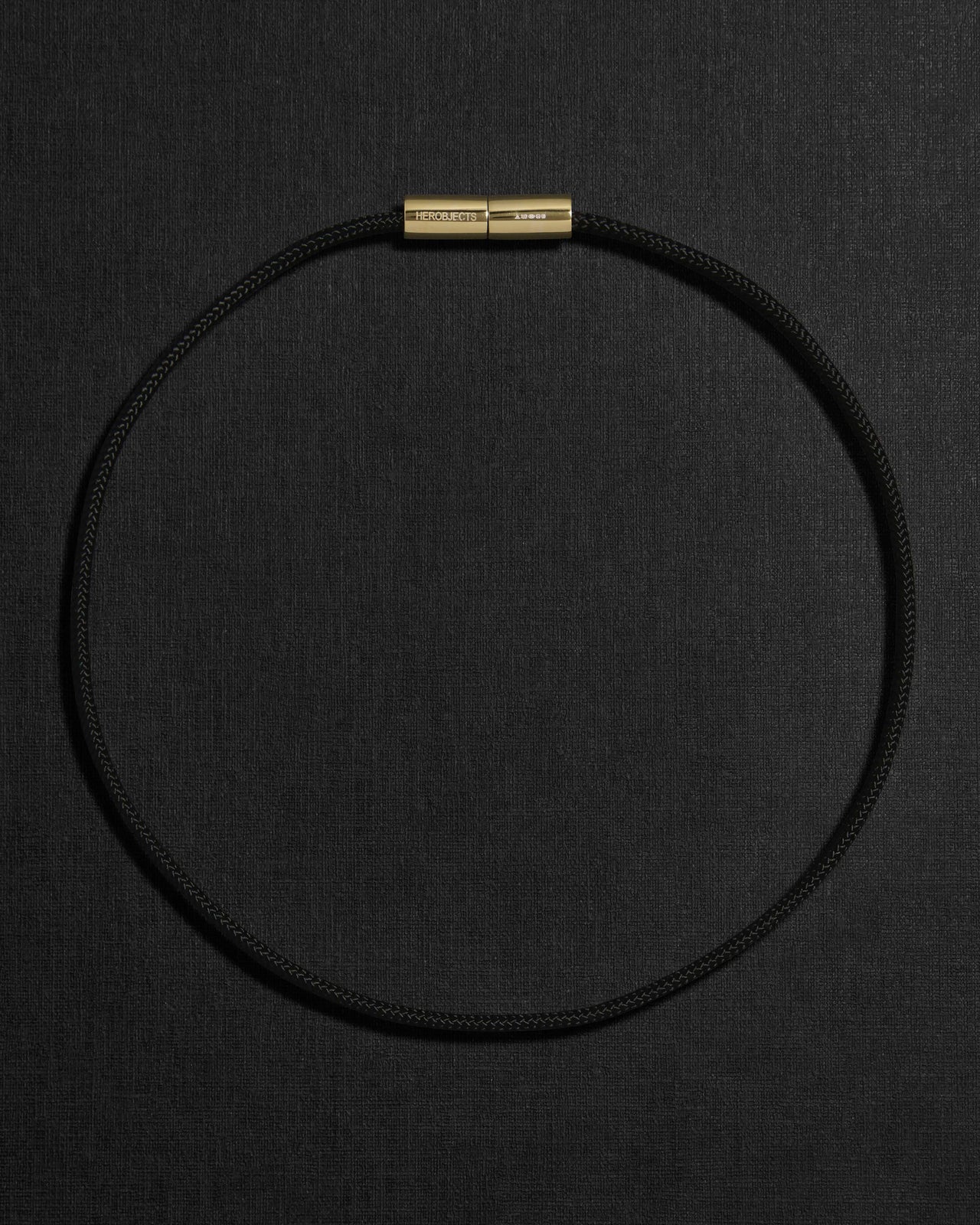 Black cord necklace with a 18K gold clasp on a black background
