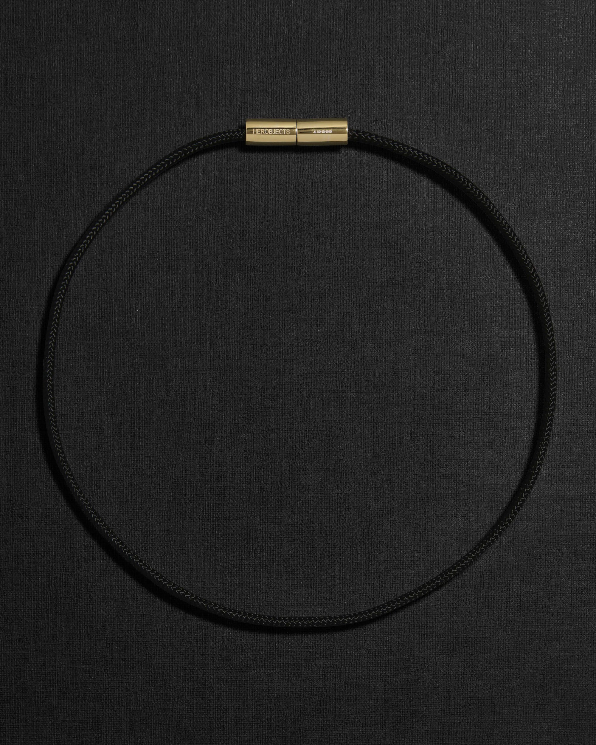 Black cord necklace with a 18K gold clasp on a black background