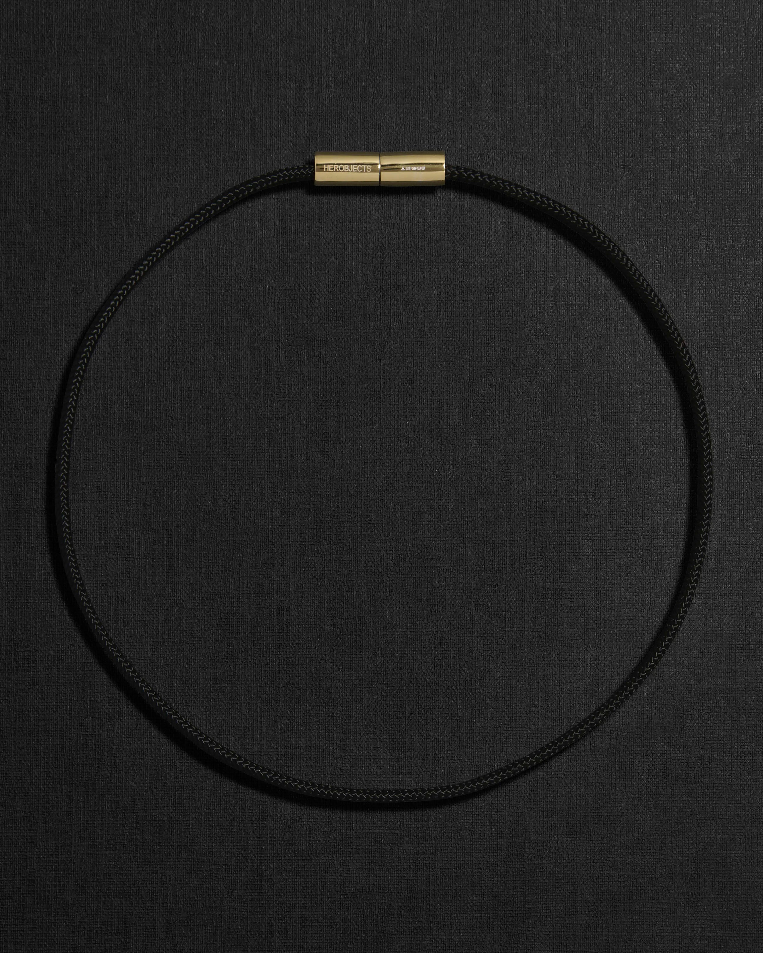 Black cord necklace with a 18K gold clasp on a black background
