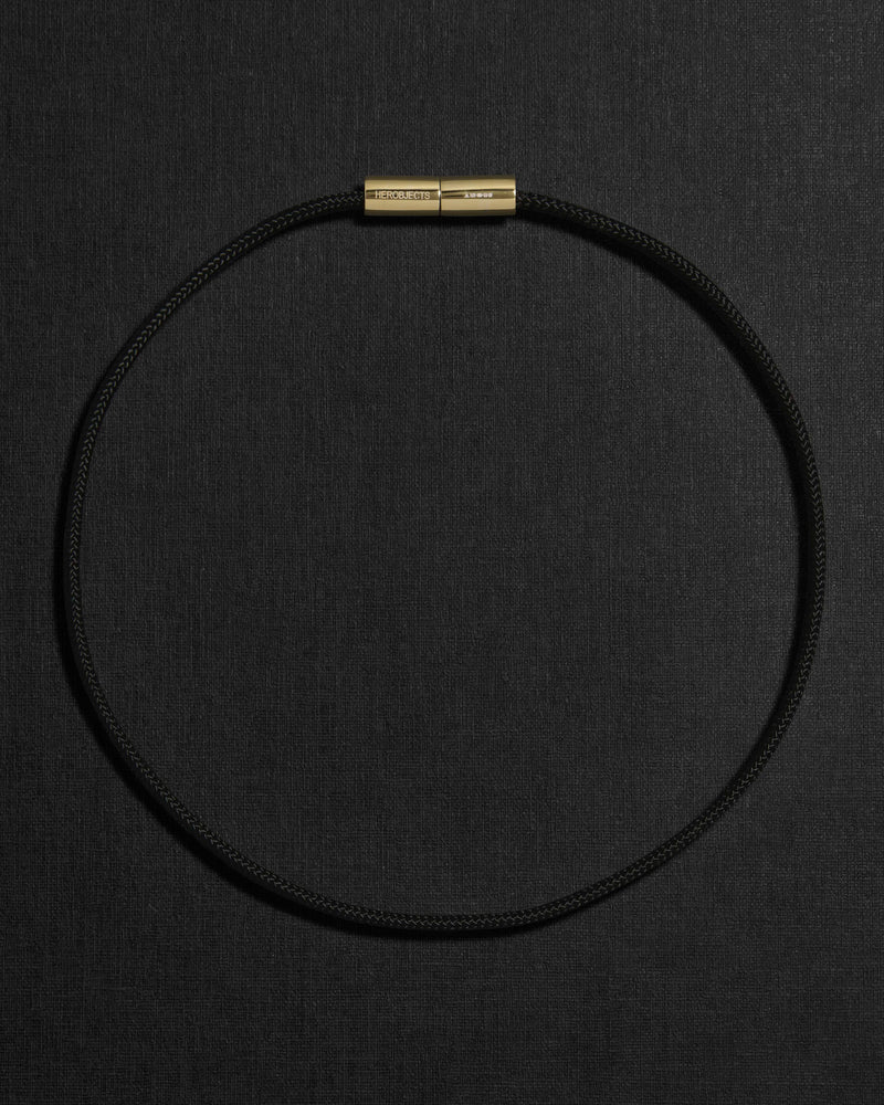 Black cord necklace with a 18K gold clasp on a black background