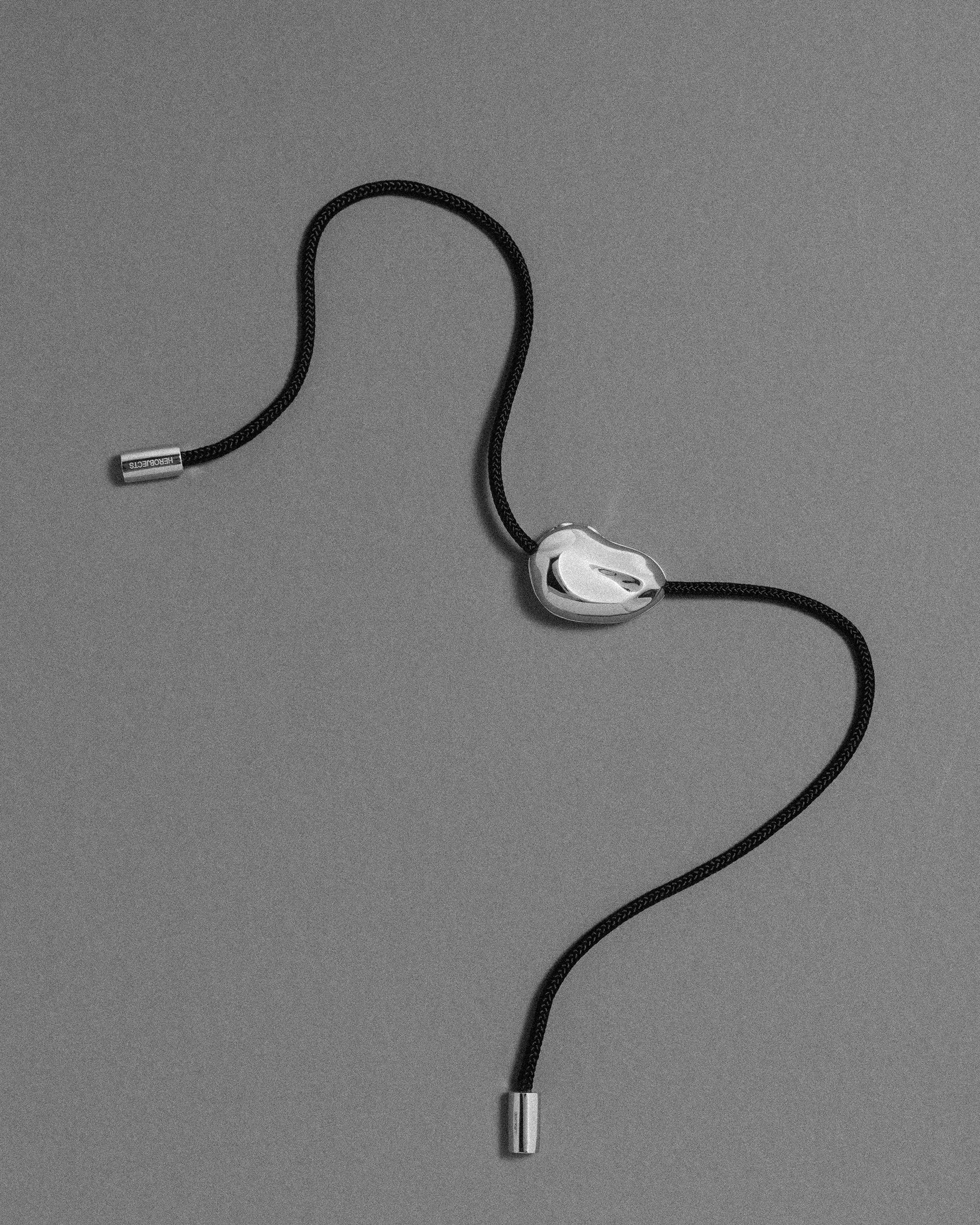 Black cord necklace with a 18K gold clasp and 18K gold pomegranate-shaped pendant on a grey background