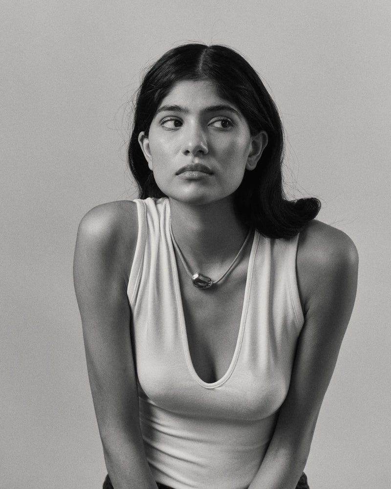 Black and white portrait of a model wearing a 18K gold blue cord necklace and pomegranate-shaped pendant