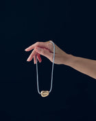 Hand holding a 18K gold blue cord necklace with a 18K gold heart-shaped pendant against a black background