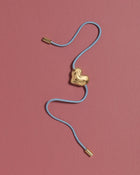 Blue cord necklace with a 18K gold clasp and a heart-shaped 18K gold pendant on a pink background