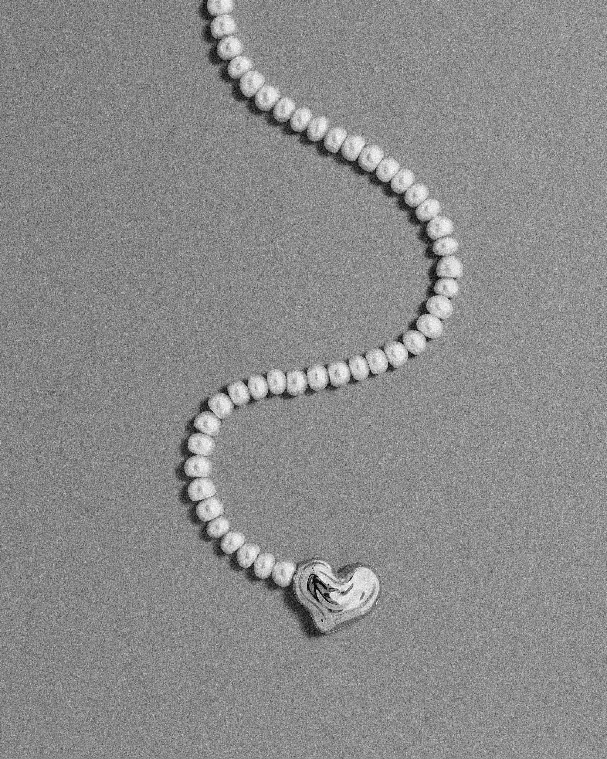 18K gold blush pearl necklace with a heart-shaped 18K gold pendant on a grey background