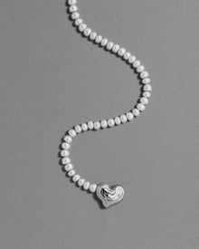 18K gold blush pearl necklace with a heart-shaped 18K gold pendant on a grey background