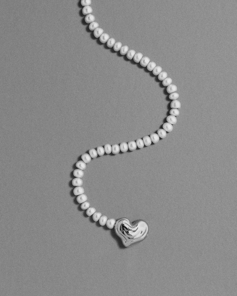18K gold blush pearl necklace with a heart-shaped 18K gold pendant on a grey background