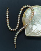 Blush pearl necklace with a 18K gold clasp on a dark surface with a large shell
