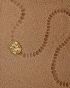 18K Gold Hero Desert pendant on a sand