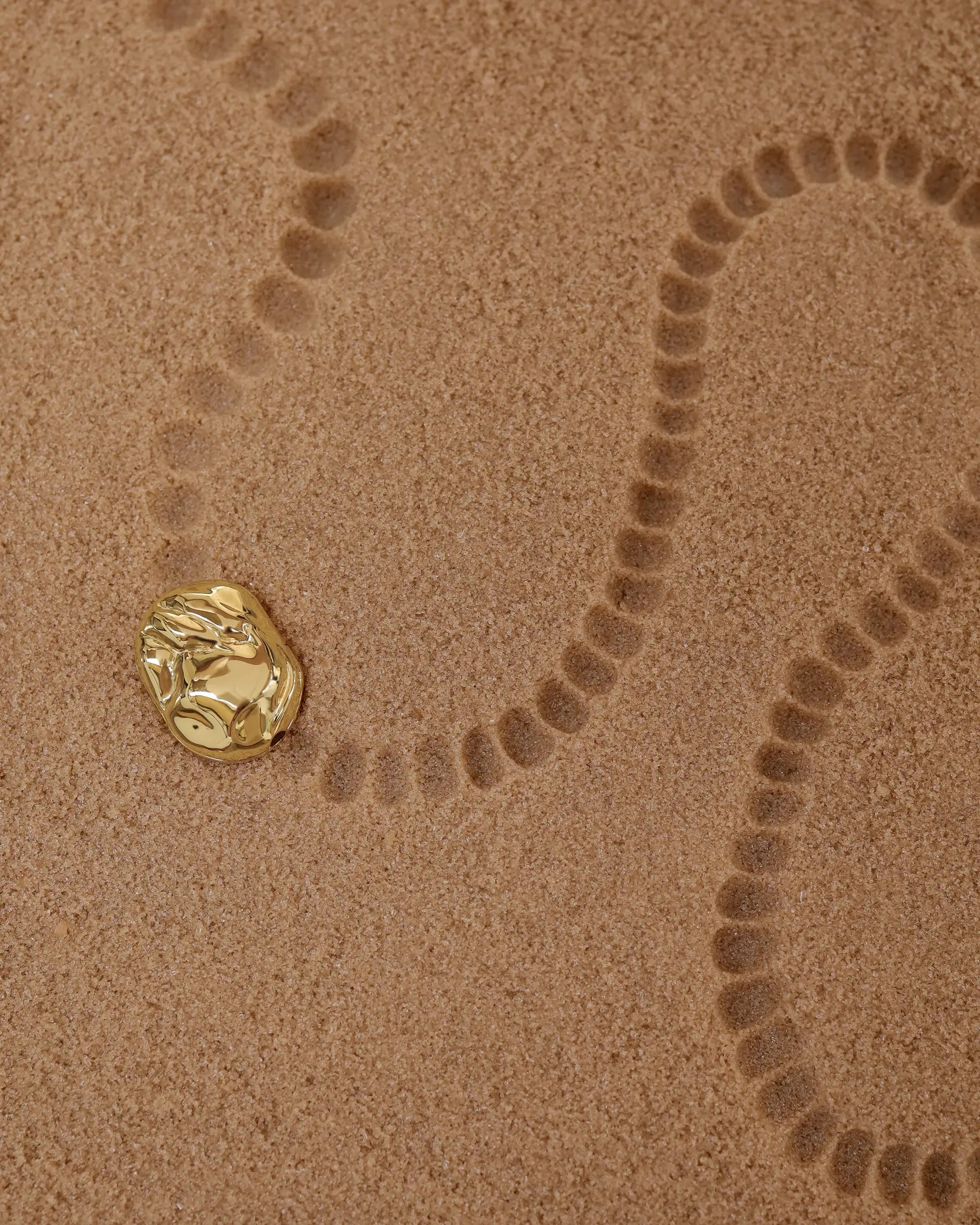 18K Gold Hero Desert pendant on a sand