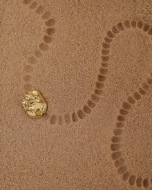 18K Gold Hero Desert pendant on a sand