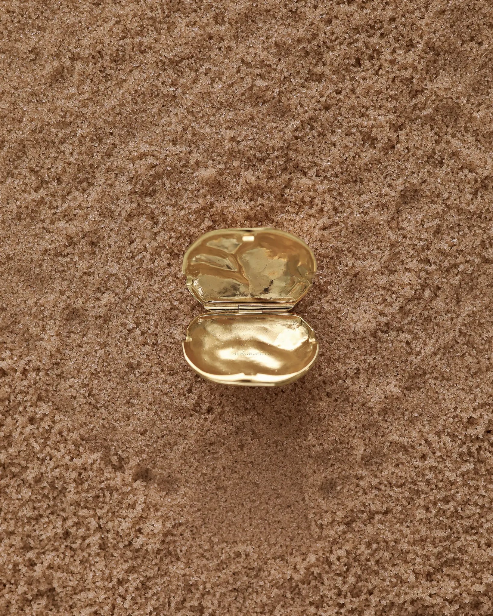 Opened 18K Gold Hero Desert pendant on a sand