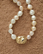 18K Gold Hero Desert pendant and 18K Gold large ivory baroque pearl on a sand