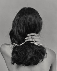Model with long dark hair wearing a 18K gold grey pearl necklace and 18K gold pendant against a plain background