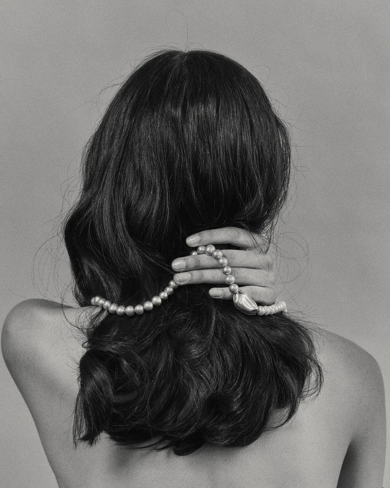 Model with long dark hair wearing a 18K gold grey pearl necklace and 18K gold pendant against a plain background
