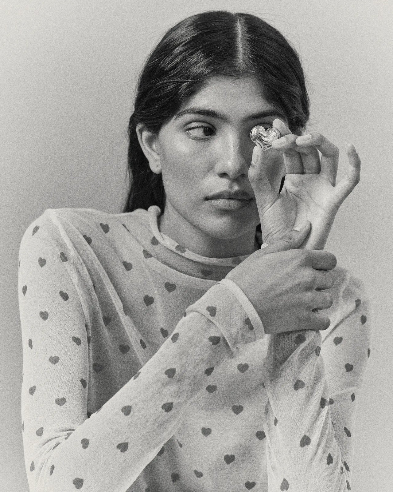 Model holding heart-shaped 18K gold pendant on a grey background