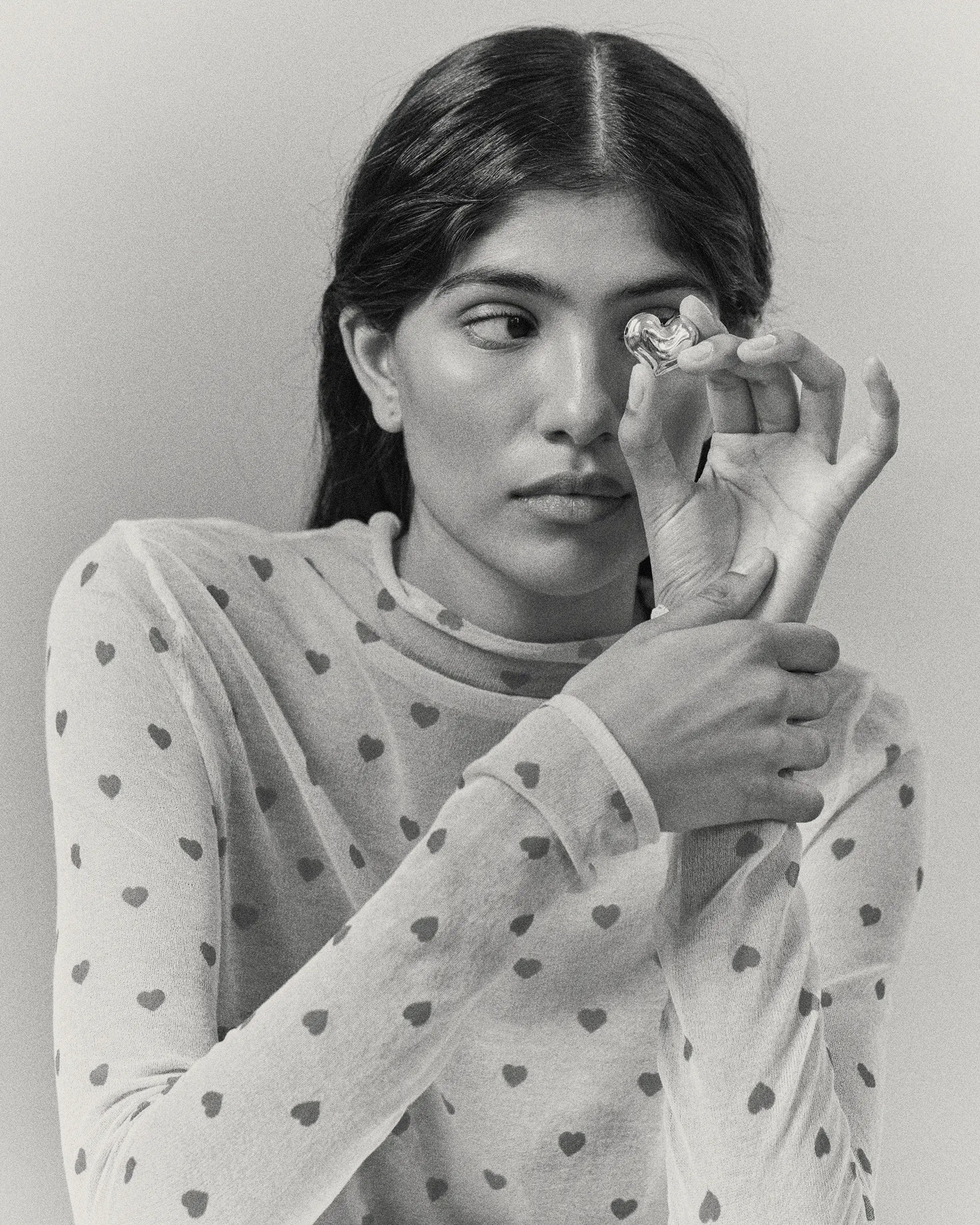Model holding heart-shaped 18K gold pendant on a grey background