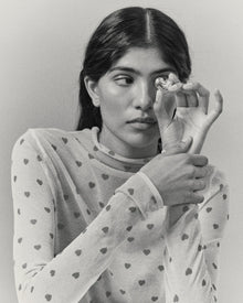 Model holding heart-shaped 18K gold pendant on a grey background