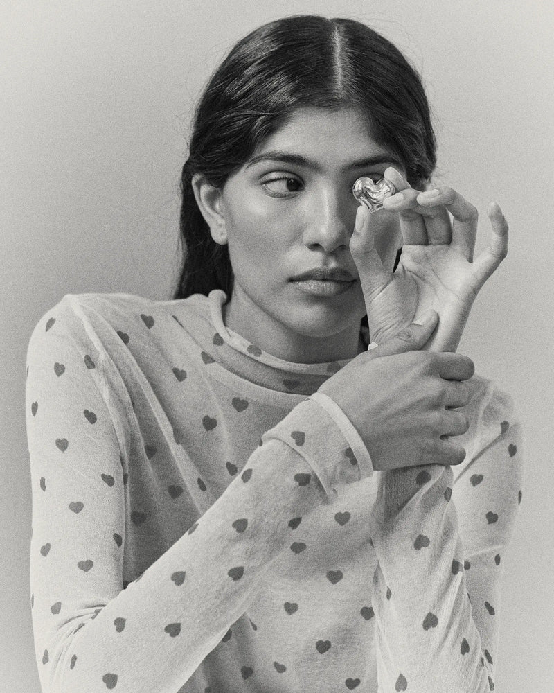 Model holding heart-shaped 18K gold pendant on a grey background