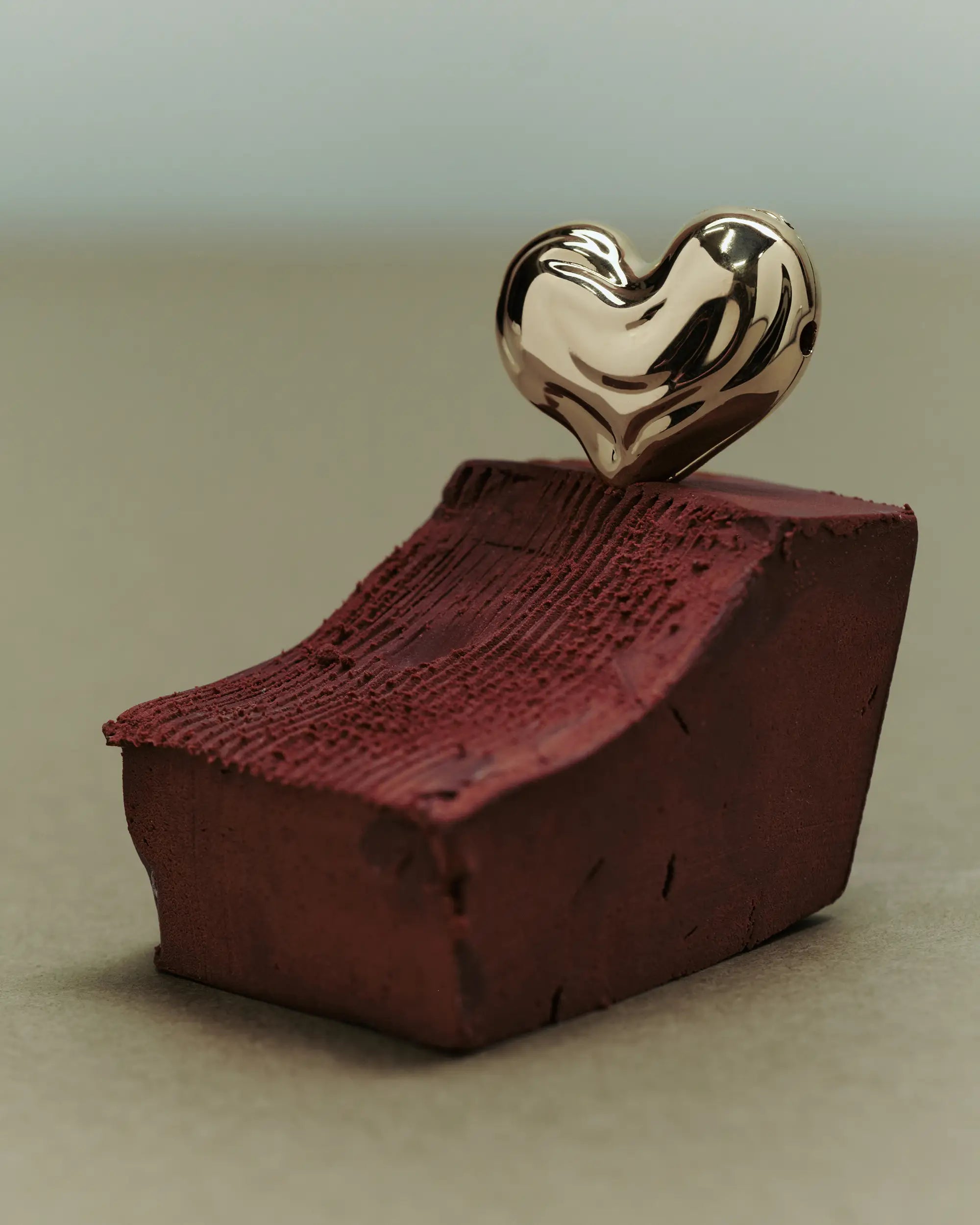 Red clay block with a heart-shaped 18K gold pendant on top against beige background