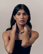 Model wearing 18K gold black pearl necklace and heart-shaped 18K gold pendant on a beige background