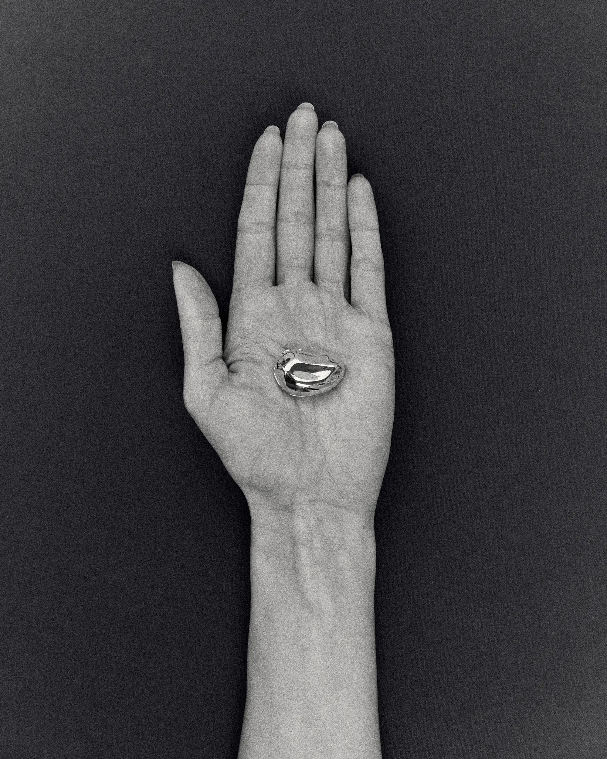 Hand holding pomegranate-shaped 18K gold pendant on a black background