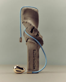 Decorative object with a 18K gold blue cord and pomegranate-shaped 18K gold pendant on a beige background
