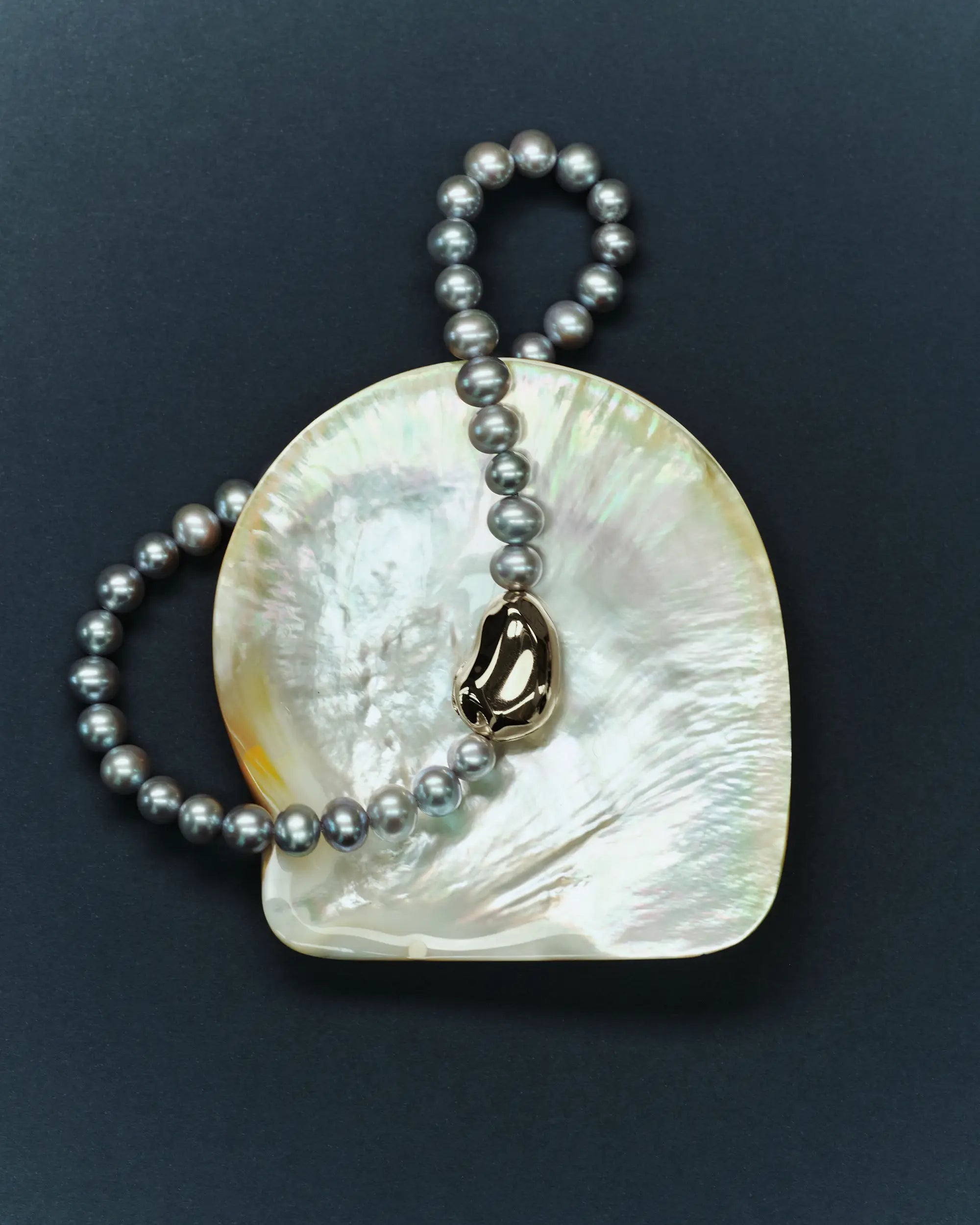 18K gold grey pearl necklace and pomegranate-shaped 18K gold pendant with a shell on a dark blue background