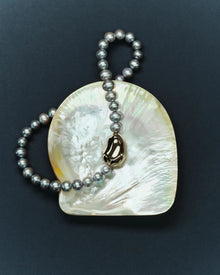 18K gold grey pearl necklace and pomegranate-shaped 18K gold pendant with a shell on a dark blue background