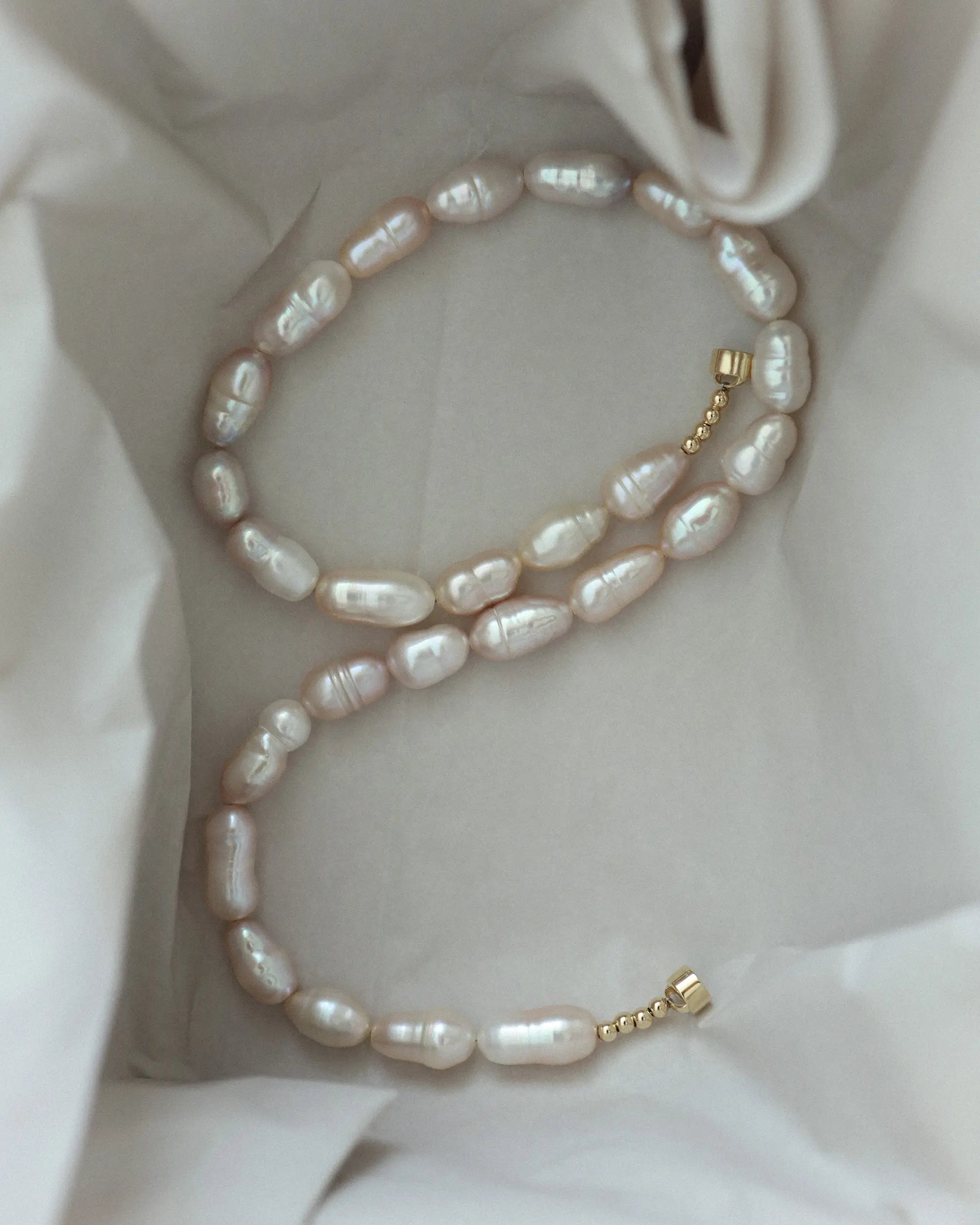 A strand of irregular 18K gold lavender baroque pearls, arranged inside the box.