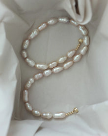 A strand of irregular 18K gold lavender baroque pearls, arranged inside the box.