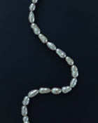 A strand of irregular baroque freshwater pearls draped in a curved S-shape against a solid blue background.