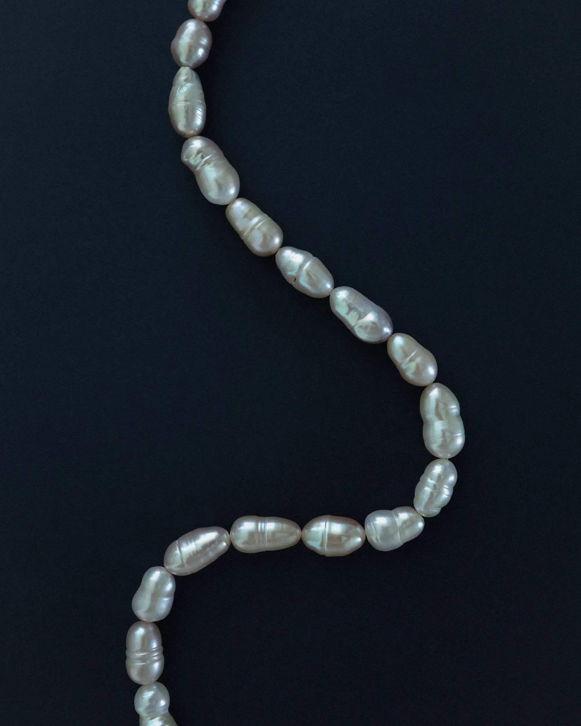 A strand of irregular baroque freshwater pearls draped in a curved S-shape against a solid blue background.