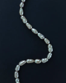 A strand of irregular baroque freshwater pearls draped in a curved S-shape against a solid blue background.