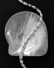 A close-up of a translucent white shell with a curved, scalloped edge, draped with a strand of irregular white pearls, set against a solid black background.