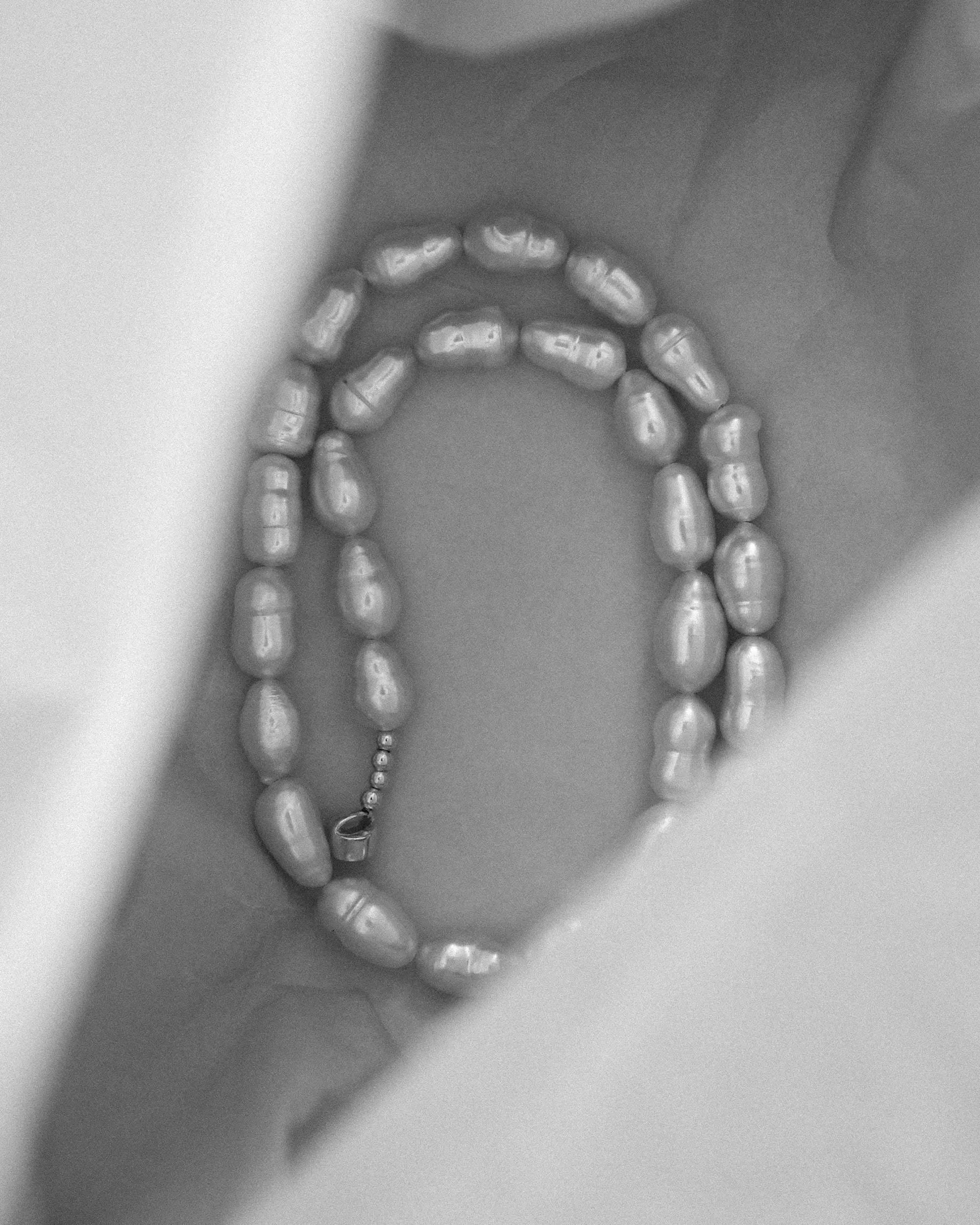 A strand of irregular 18K gold lavender baroque pearls, arranged inside the box.