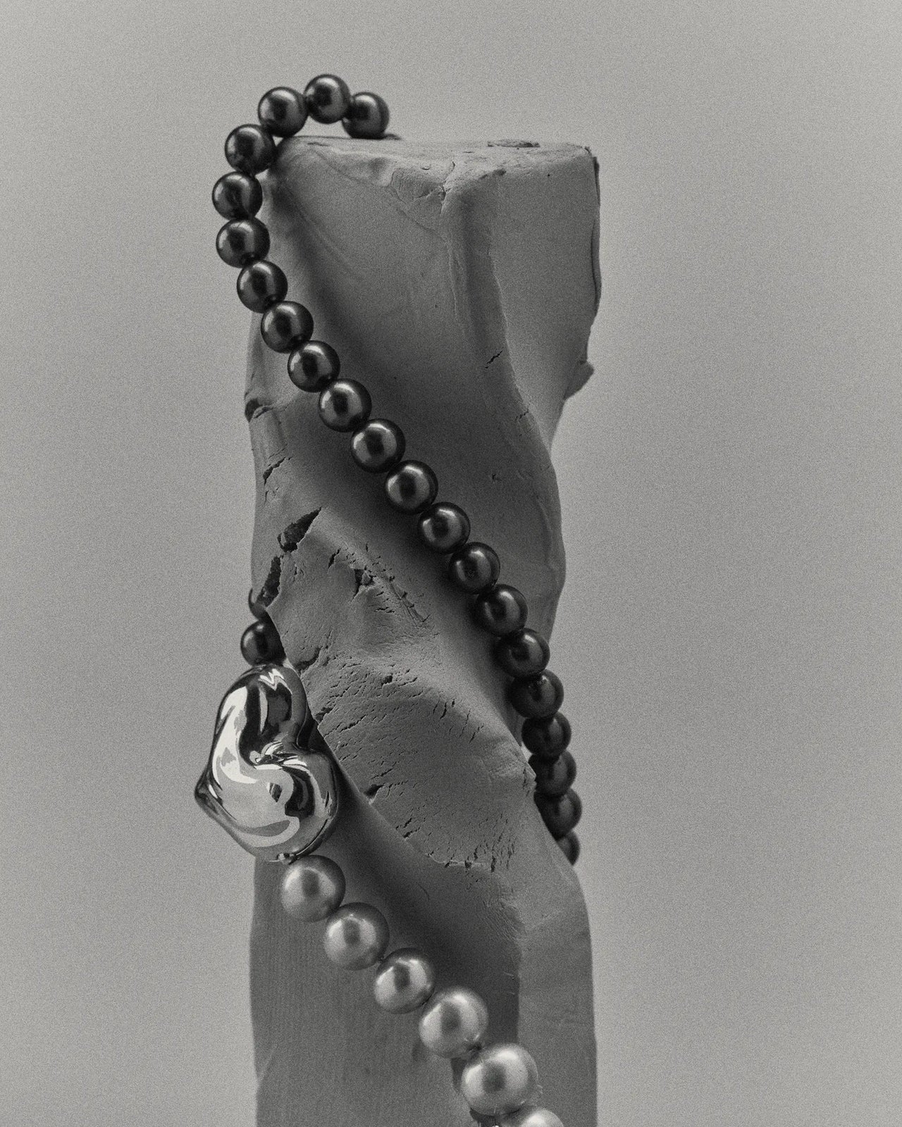 18K gold black pearl necklace with a 18K gold heart-shaped pendant on a clay sculpture